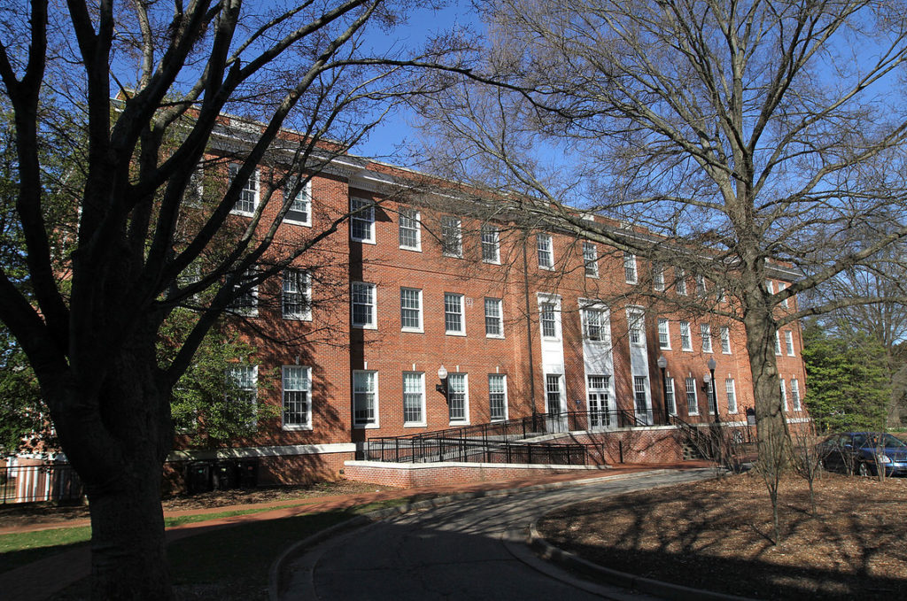 Multi-story brick building with large trees in front. 