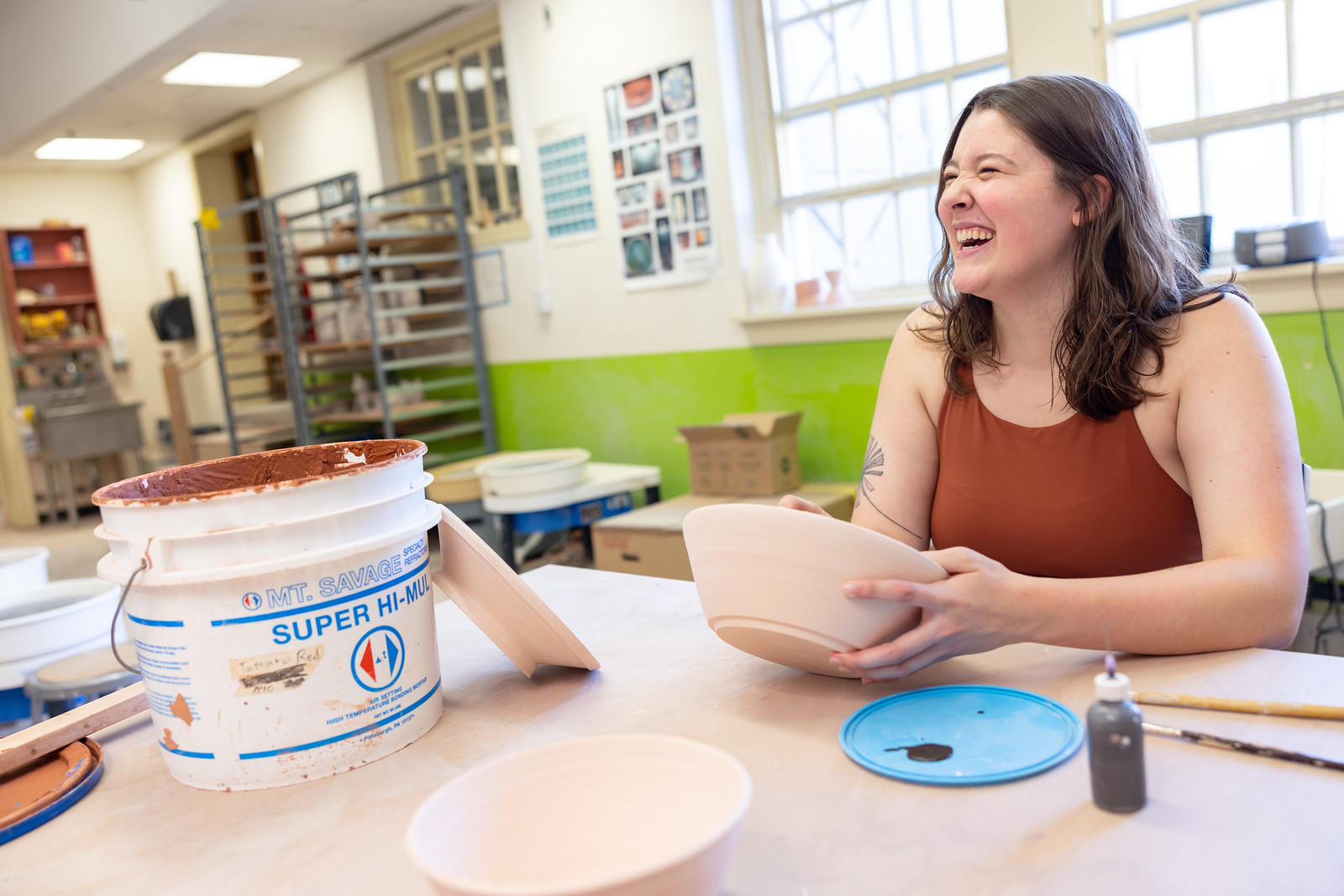 student laughing and smiling while holding a ceramic bowl