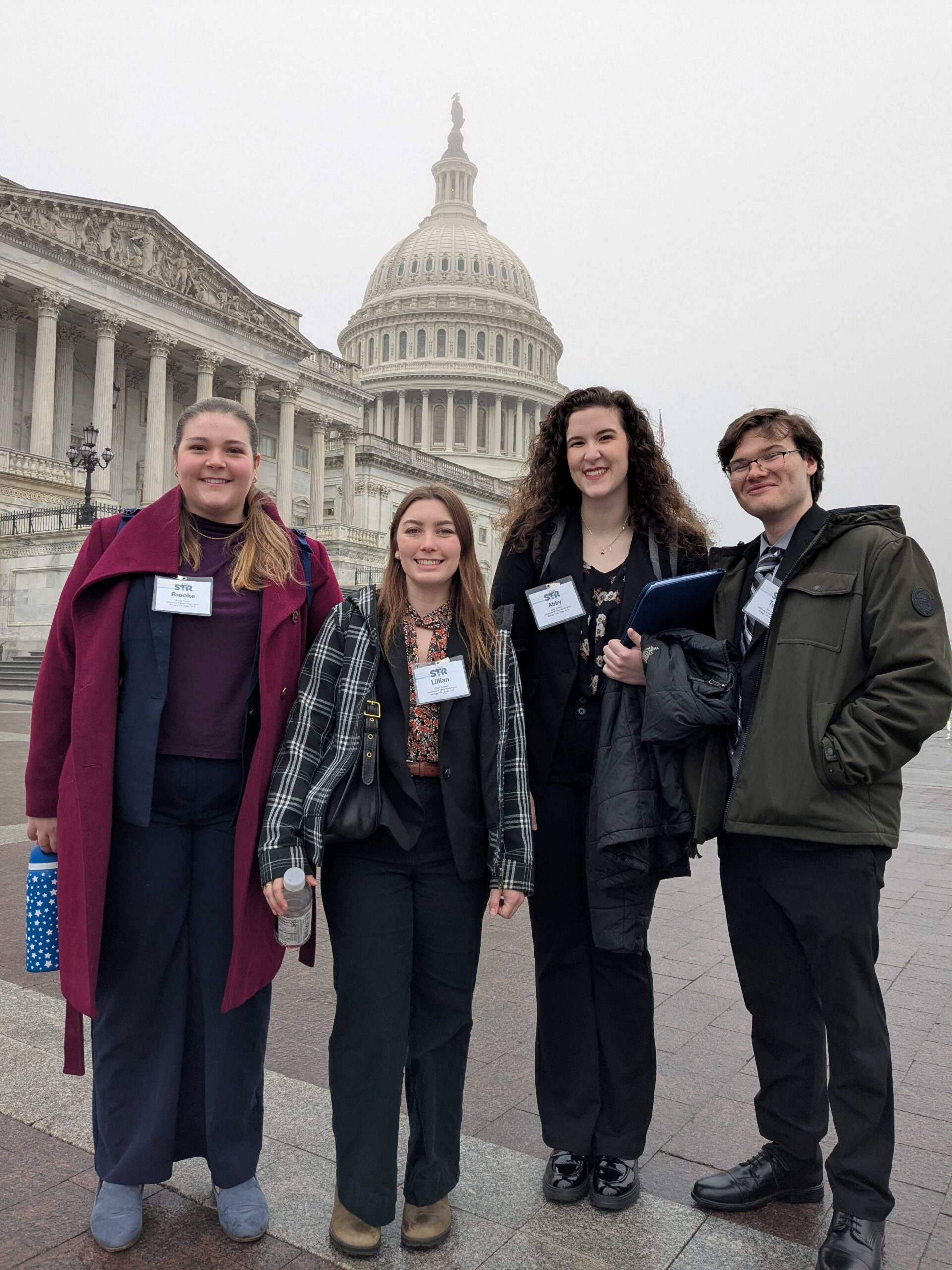 Students pose outside on the steps of the capitol with the capitol dome in the background