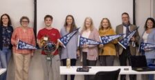 A group of faculty with a student standing in front of a classroom. The student is being congratulated for winning the Goldwater scholarship. The faculty are holding UMW pennants.