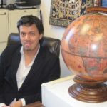Professor Barrenechea sits in in office with a globe in the foreground.