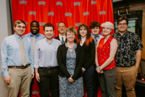 Photo of the UMW Debate Team Posing against UNLV Backdrop with Coach Adrienne Brovero
