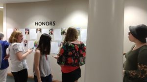 Students stand before images and paper posted on a wall under the text Honors.