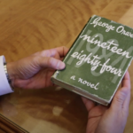 Barrenechea holds a copy of George Orwell's 1984, which is written in white text with the number spelled out on an olive green background. No other images appear on the book cover.