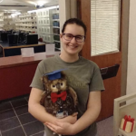 A smiling Madison Roberts poses with the Simpson OWL with library book shelves in the background.