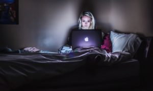 young woman sitting on bed working on computer