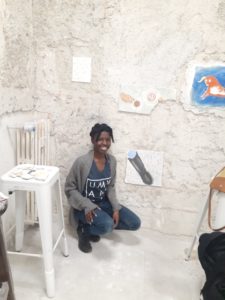 Nina Burges in a white artsy room surrounded by fresco paintings.