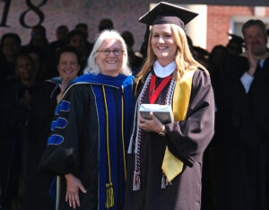 Kendall Parker in regalia with her award at commencement next to Provost Nina Mikhalevsky. The audience is clapping.