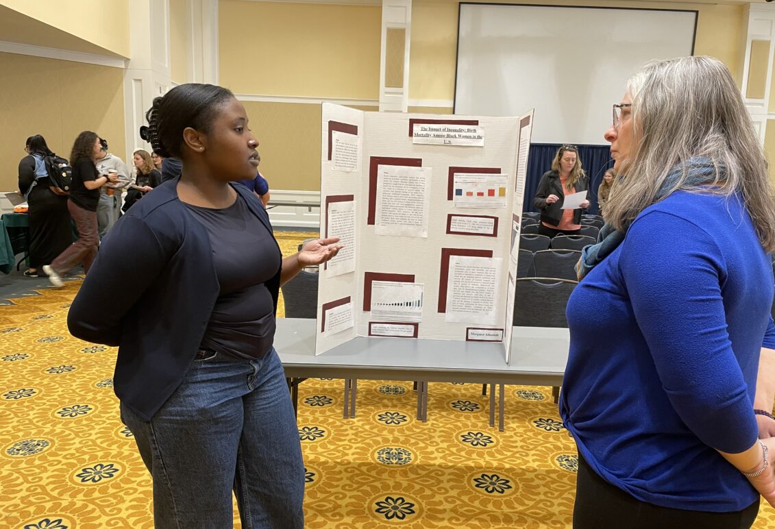 A person presenting in front of a trifold poster board. 
